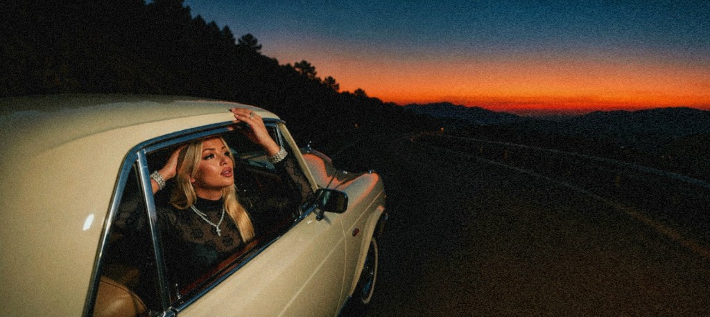 Amber Della Vita in a white vintage convertible at sunset